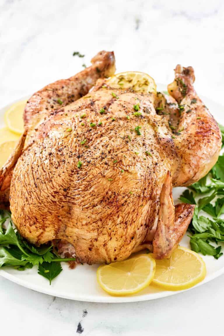 Whole oven roasted chicken, lemon slices, and fresh herbs on a round platter.