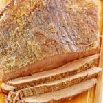 Oven baked beef brisket on a cutting board and a meat fork next to it.