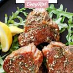 Three pan seared lamb chops, two lemon wedges, and arugula on a plate.