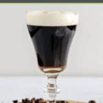 Traditional Irish coffee in a tulip stem glass and coffee beans around it.