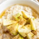 A bowl of oatmeal with cinnamon and apples on top.