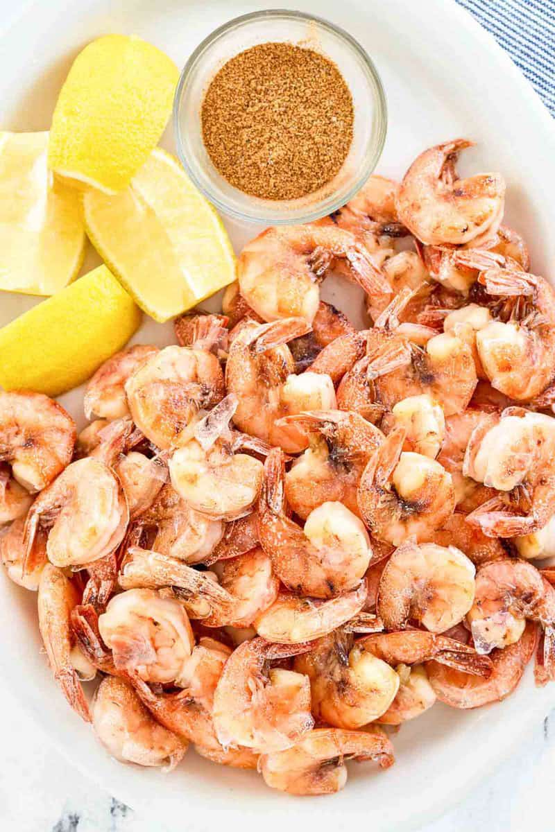 Freshly boiled shrimp with shells and lemon wedges on a platter.