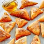 A bunch of homemade Mexican sopapillas and a small cup of honey.