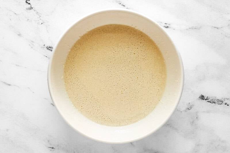An overhead shot of the finished Applebee's oriental salad dressing in a white bowl on a marble surface. The creamy, light-beige dressing has been whisked until smooth and has small bubbles on the surface.
