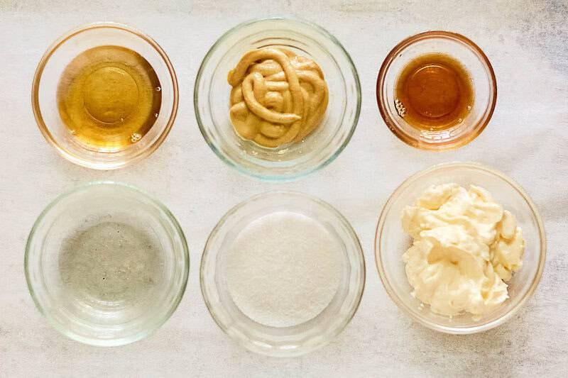 An overhead view of the ingredients for Applebee's oriental salad dressing arranged in small glass bowls. Pictured are bowls of rice vinegar, Dijon mustard, toasted sesame oil, sugar, and mayonnaise, along with an empty bowl for another oil.