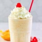 Copycat Chick-fil-A peach milkshake in a tall glass, peach slices, and cherries.