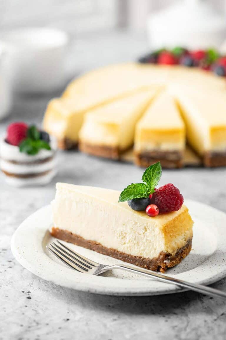 New York style cheesecake slice on a plate and the cheesecake behind it.