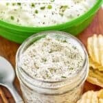 Homemade dry ranch dressing mix in a small glass jar next to a bowl of ranch dip.