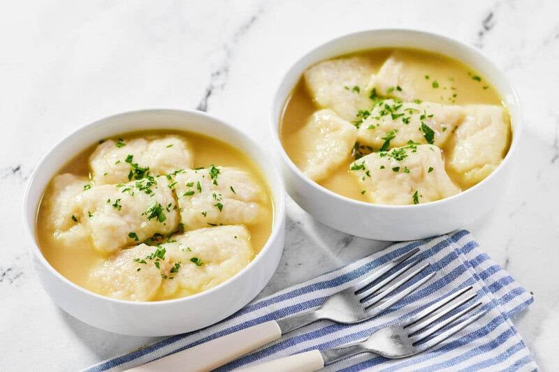 Two bowls of tender dumplings in savory broth, garnished with parsley, placed next to silver forks on a blue and white napkin.