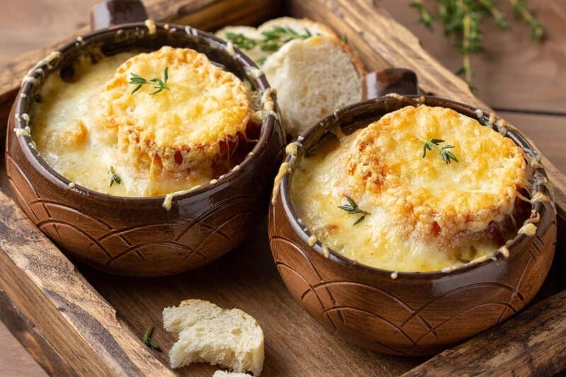 Two bowls of homemade classic French onion soup and pieces of bread.
