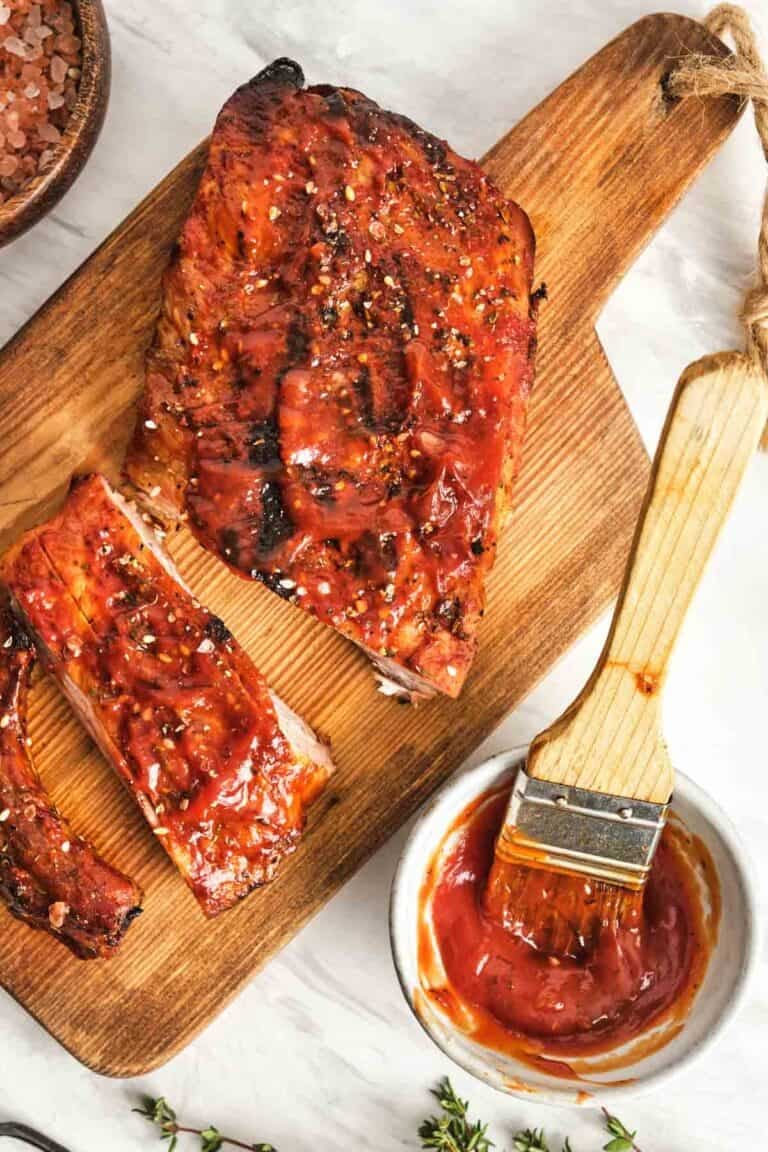 Homemade St. Louis style barbecue sauce in a small cup and on a rack of ribs.