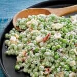 Homemade pea salad with bacon and cheese and a wooden spoon on a plate.