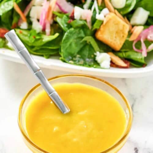 Copycat Simon and Seafort's mustard dressing in a small bowl and a salad behind it.