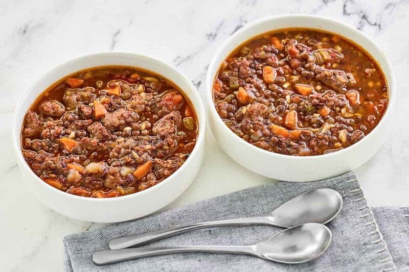 Two bowls of copycat Carrabba's sausage and lentil soup and two spoons in front of them.