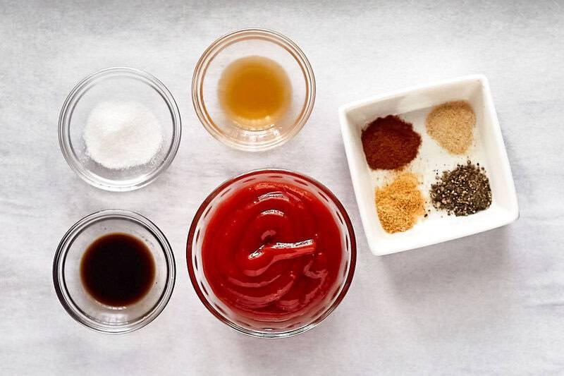 An overhead view of the ingredients for Arby's Red Ranch Sauce. Pictured are bowls of ketchup, apple cider vinegar, Worcestershire sauce, and sugar, along with a dish containing mounds of garlic powder, onion powder, smoked paprika, and black pepper.