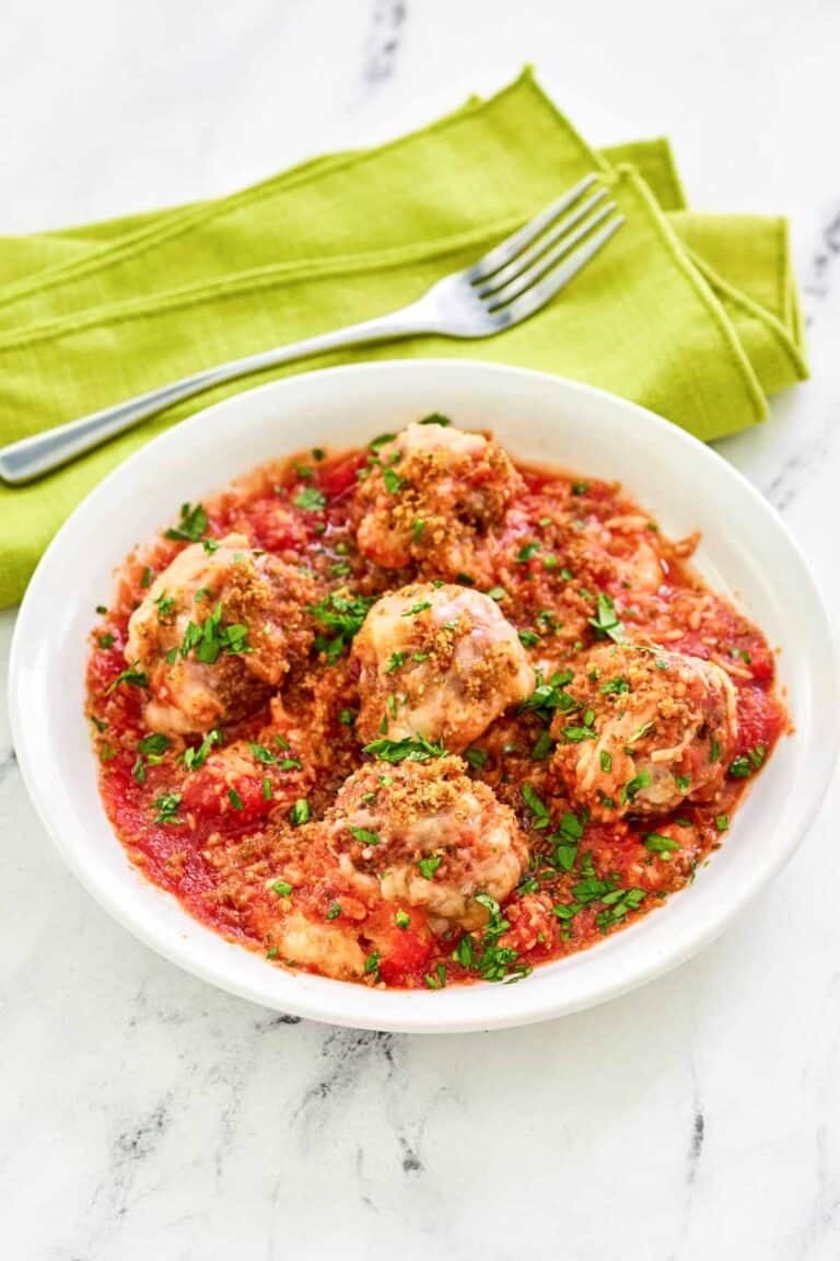 Copycat Olive Garden meatballs parmigiana and a fork on a napkin behind it.