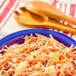 A bowl of Chick-fil-A carrot and raisin salad, wooden salad servers, and kitchen towel.