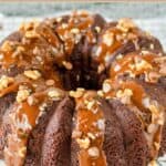 Homemade triple chocolate bundt cake topped with fudge sauce and chopped pecans.