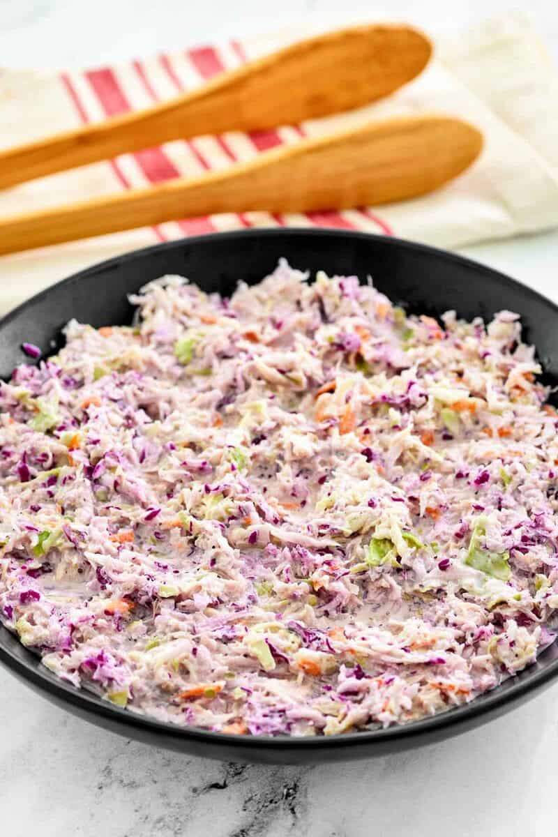 A bowl of copycat Famous Dave's coleslaw and wooden serving tongs behind it.
