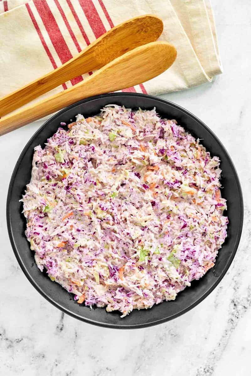 Copycat Famous Dave's coleslaw in a serving bowl and wooden tongs on a cloth napkin.