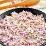 Homemade Famous Dave's coleslaw in a large bowl and wooden tongs behind it.