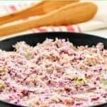 Homemade Famous Dave's coleslaw in a serving bowl and wooden serving tongs behind it.