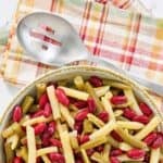 A bowl of Grandma's three bean salad and a slotted spoon on a napkin.