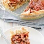 Homemade karo syrup pecan pie slice on a plate and the pie behind it.