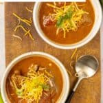 Two bowls of Lady Bird Johnson's Pedernales river chili and a spoon on a wooden board.