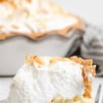 A slice of copycat Luby's coconut meringue pie on a plate and the pie behind it.