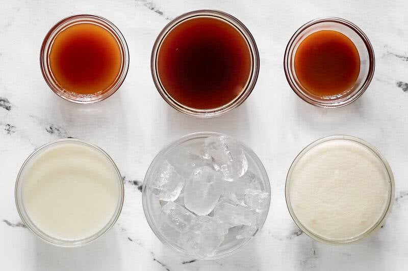 Six glass bowls show the ingredients for a McDonald's caramel frappe: coffee, caramel syrup, milk, ice, and a creamy base, seen from above.
