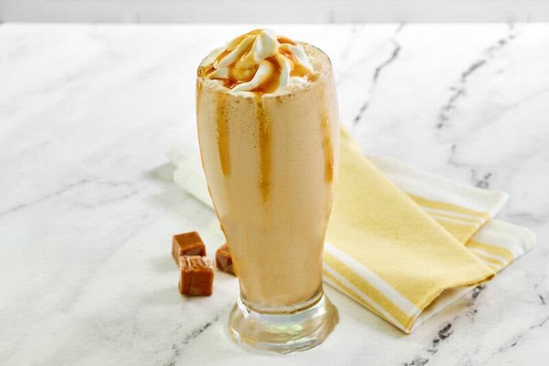 A finished copycat McDonald's caramel frappe in a tall glass with whipped cream and caramel drizzle, next to a yellow towel..