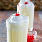 Copycat McDonald's eggnog shake in two tall glasses and a small bowl of cherries.