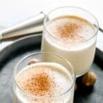 Homemade New Orleans milk punch in two glasses on a round tray.