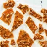 Homemade pecan brittle scattered on parchment paper.