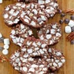 Homemade rocky road candy, marshmallows, chocolate chips, and pecans on a wood board.