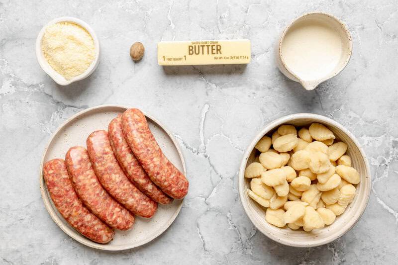 Creamy alfredo sausage and gnocchi bake ingredients on a marble surface.