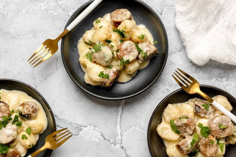 Three servings of creamy alfredo sausage and gnocchi bake and a fork on each one.