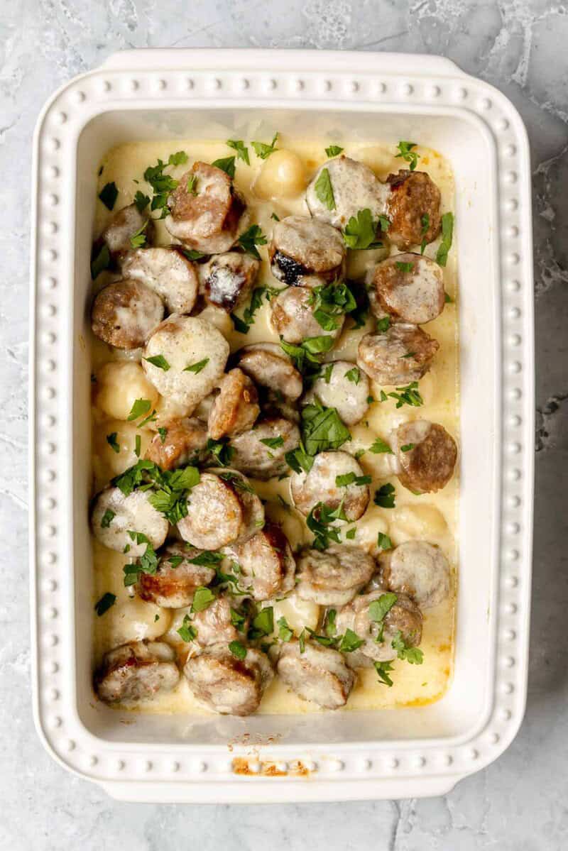 Creamy alfredo sausage and gnocchi bake in a casserole dish on a marble surface.