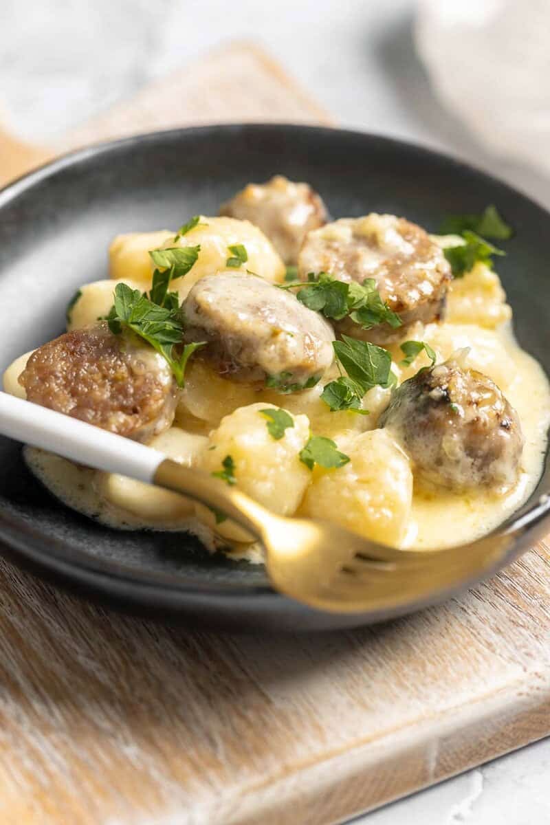Creamy alfredo sausage and gnocchi bake on a plate on a wood surface.
