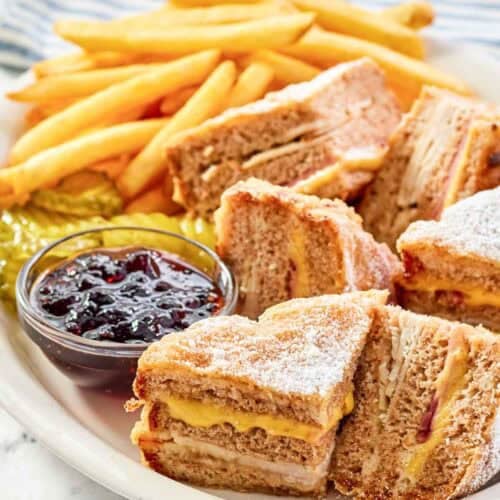 Copycat Bennigan's monte cristo sandwich slices, raspberry jam, fries, and pickles on a platter.