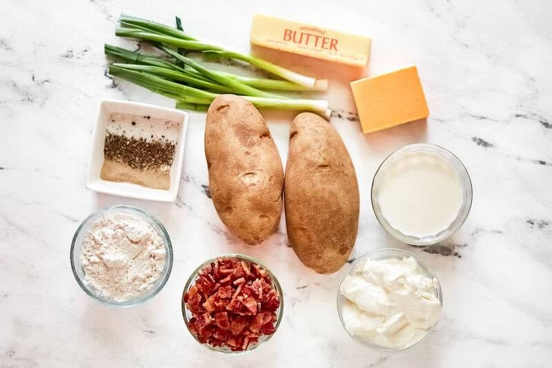 An overhead view of potato soup ingredients: russet potatoes, butter, cheese, bacon, green onions, sour cream, milk, and flour.