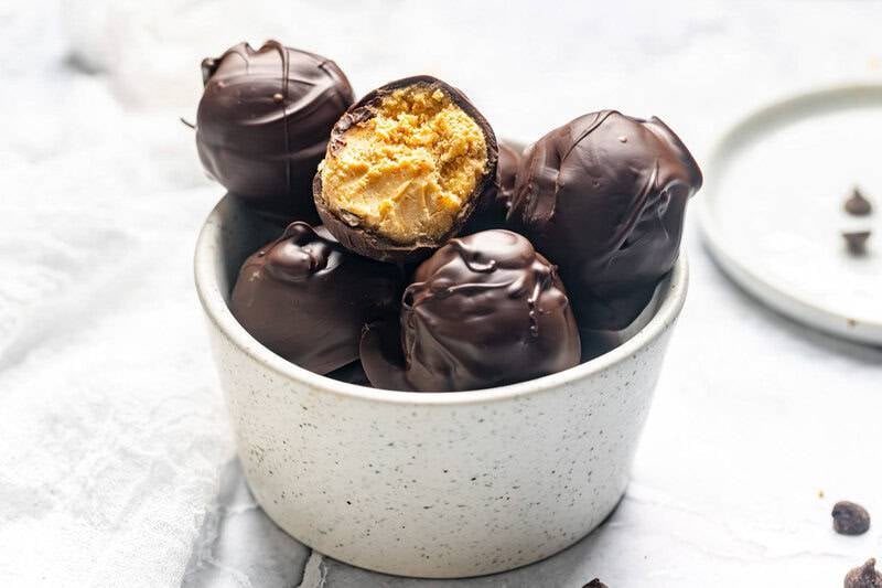 Homemade chocolate peanut butter balls in a bowl and chocolate chips scattered by it.