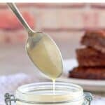 Homemade sweetened condensed milk in a glass jar and dripping from a spoon.