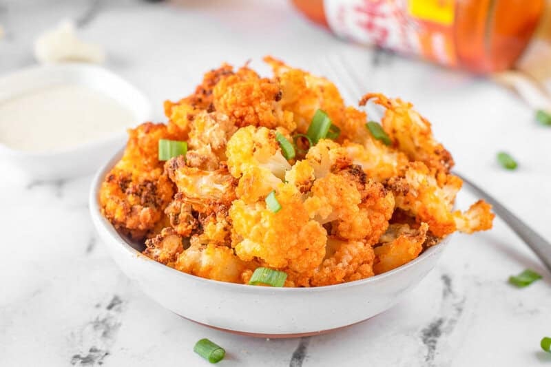 Air fryer buffalo cauliflower and dipping sauce on a marble surface.