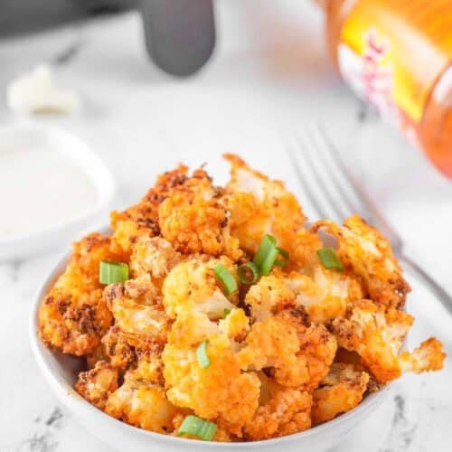 Air fryer buffalo cauliflower garnished with green onions on a marble surface.
