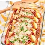 Homemade four cheese manicotti in a glass baking dish and a wooden spatula behind it.