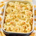 Creamy, cheesy cauliflower au gratin in a casserole dish resting on a kitchen towel.