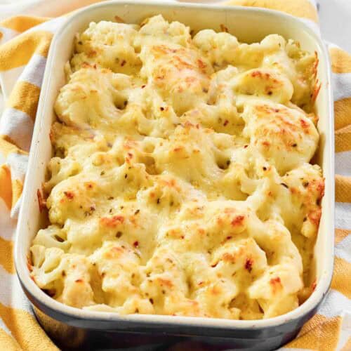 Creamy, cheesy cauliflower au gratin in a casserole dish resting on a kitchen towel.