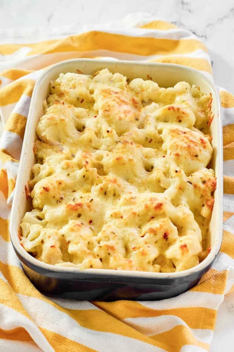 Creamy, cheesy cauliflower au gratin in a casserole dish resting on a kitchen towel.